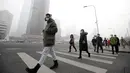 Sejumlah warga berjalan mengenakan masker saat beraktivitas di distrik Beijing pusat bisnis, Tiongkok, (21/12). Kabut asap akibat polusi udara yang melanda sebagian kota-kota di Tiongkok membuat warga beraktivitas mengunakan masker. (Reuters/Jason Lee)