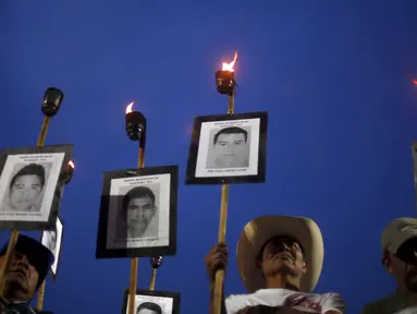 Kerabat membawa obor dan poster bergambar wajah 43 mahasiswa yang menghilang, ketika long march di jalanan Meksiko City, Selasa (26/4). Mereka mendesak pemerintah segera menangani kasus yang sudah 19 bulan berlalu tersebut. (REUTERS/Edgard Garrido)