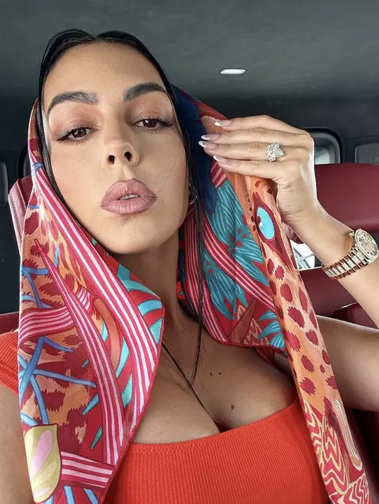 Dress merah tersebut dipadukan scraf colorfull untuk menutupi kepalanya. Nampak cincin berlian terlihat ia kenakan di jarinya serta jam tangan mewahnya. Credit:  (@georginagio)