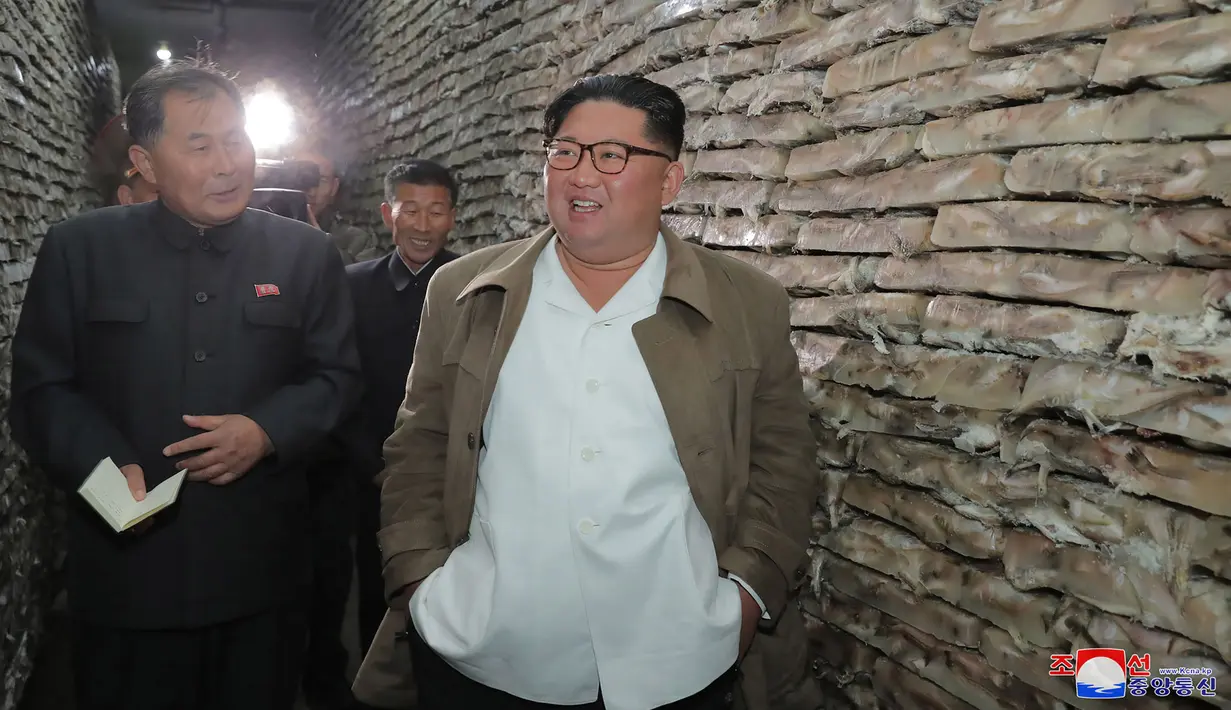 Gambar tak bertanggal yang dirilis pada 19 November 2019, pemimpin Korea Utara Kim Jong-un (kanan) mengunjungi pabrik pengolahan ikan di lokasi yang dirahasiakan di Korea Utara. Kim Jong-un berbicara dengan para pekerja dan sesekali tertawa saat berkeliling pabrik.  STRINGER/KCNA VIA KNS/AFP)