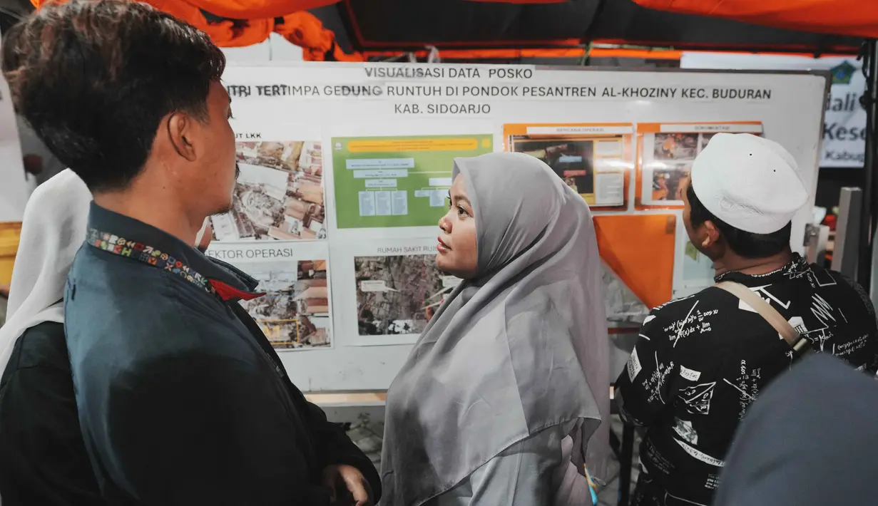 Keluarga santri memeriksa papan informasi sambil menunggu upaya penyelamatan bagi korban yang terjebak reruntuhan bangunan yang sedang dibangun di sebuah pondok pesantren di Sidoarjo, Jawa Timur, Rabu 1 Oktober 2025. (AP Photo/Achmad Ibrahim)
