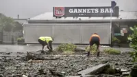 Para pria membersihkan puing-puing dengan tangan di jalan yang terendam banjir di Te Awanga, tenggara Auckland, Selandia Baru, Selasa (14/2/2023). Badai topan Gabrielle itu sendiri merupakan peristiwa cuaca besar kedua yang melanda Auckland dan North Island hanya dalam beberapa pekan terakhir. (Warren Buckland/Hawkes Bay Today via AP)