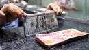 Pelemahan mata uang rupiah terhadap dollar AS dipengaruhi eskalasi di Kawasan Timur Tengah yang semakin memanas. Tampak dalam foto, karyawan menunjukkan uang pecahan dolar Amerika Serikat (AS) dan rupiah di salah satu gerai penukaran mata uang asing, Jakarta, Rabu (5/5/2026). (Kapanlagi.com/Budy Santoso)