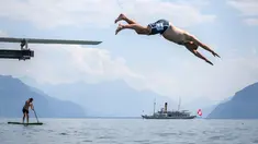 Seorang pria melompat ke Danau Jenewa di Saint Saphorin, Swiss barat saat gelombang panas melanda seluruh Eropa utara (31/7). Akibat gelombang panas suhu di beberapa bagian Swiss mencapai 35 Derajat. (AFP Photo/Fabrice Coffrini)