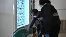 Seorang pria menggunakan mesin penjual otomatis (vending machine) yang menyediakan alat test kit COVID-19 di stasiun kereta bawah tanah MTR di Hong Kong, Senin (7/12/2020). Mesin penjual otomatis tersebut akan memasok 10.000 alat tes COVID-19 dalam sehari. (Anthony WALLACE / AFP)