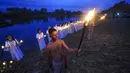 Pemuda Belarusia memegang lilin dan obor berdiri di Sungai Berezina pada Hari Ivan Kupala di Desa Parichi, sekitar 200 km (125 mil) selatan Parichi, Belarusia, 6 Juli 2022. Hari Ivan Kupala merupakan sebuah perayaan malam kuno yang menandai Titik Balik Matahari Musim Panas, malam terpendek tahun ini. (AP Photo/Viktor Drachev)