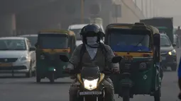 Pengendara motor mengenakan masker di tengah kondisi kabut asap tebal di New Delhi (30/10). Tingkat kabut melonjak selama musim dingin di Delhi, ketika kualitas udara sering melampaui tingkat aman Organisasi Kesehatan Dunia. (AFP Photo/Prakash Singh)