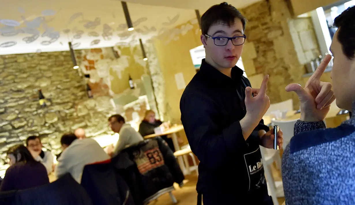 Seorang pelayan dengan down syndrome melayani pengunjung selama makan malam di restoran "Le Reflet", Nantes di Prancis Barat, 9 Februari 2017. Lelievre (26), mempekerjakan sejumlah karyawan yang memiliki down syndrome di restorannya. (LOIC VENANCE/AFP)