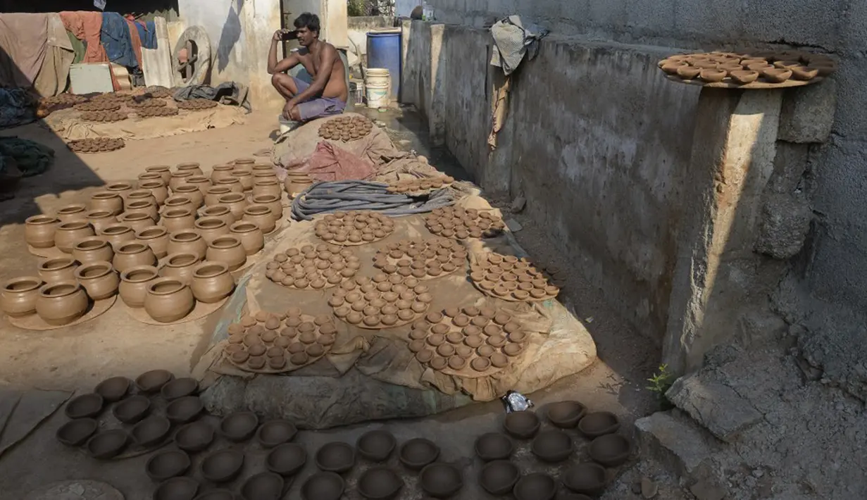Seorang pembuat tembikar berbicara lewat ponselnya usai membuat diyas atau pot minyak untuk dikeringkan di pinggiran Hyderabad, India, 26 Oktober 2021. Diwali adalah salah satu festival besar yang dirayakan oleh umat Hindu, Jain, Sikh dan beberapa umat Buddha. (NOAH SEELAM/AFP)