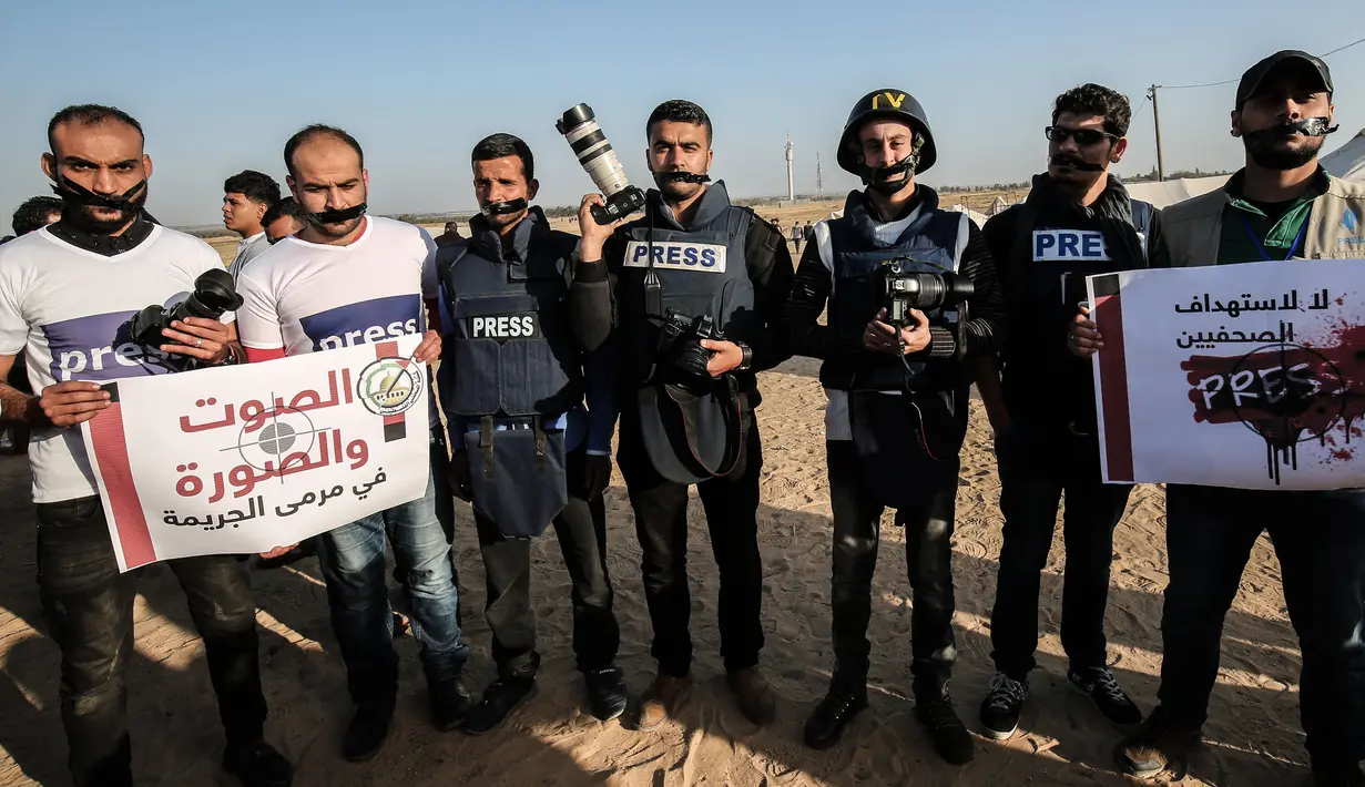 Sejumlah wartawan Palestina melakban mulut mereka saat menggelar aksi protes di dekat perbatasan Israel-Gaza, Palestina (8/4). Mereka menggelar protes terkait pembunuhan wartawan Yasser Murtaja yang mati ditembak tentara Israel. (AFP Photo/Said Khatib)