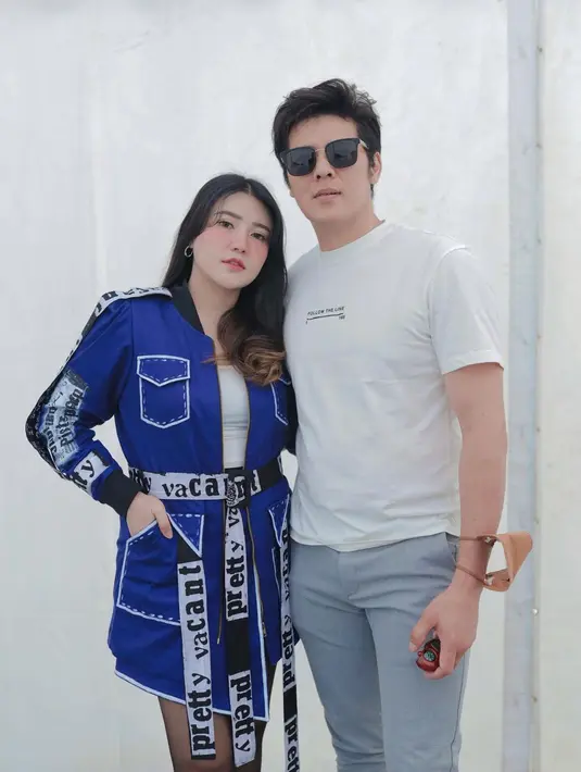 Via Vallen kembali tampil kompak dengan sang suami. Di sini, ia mengenakan mini dress lengan panjang berwarna biru dengan banyak kantong, ditambahkan dengan innerwear berwarna putih. Dress ini juga memiliki detail corak tulisan dan belt besar. Sedangkan sang suami tampil lebih kasual dengan kaus putih dan celana jeans. Foto: Instagram.