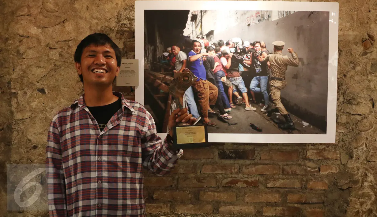Juara 1 Kategori General News, Immanuel Antonius berpose di depan karyanya berjudul "Penertiban Kampung Pulo" sambil memegang trofi Anugerah Pewarta Foto Indonesia (APFI) ke-VI di Gedung Merdeka, Bandung, Sabtu (9/4). (Liputan6.com/Immanuel Antonius)
