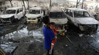 Seorang pria sambil menggendong anak melihat kondisi mobil yang hangus akibat kebakaran Depo Pertamina Plumpang (merdeka.com/Arie Basuki)
