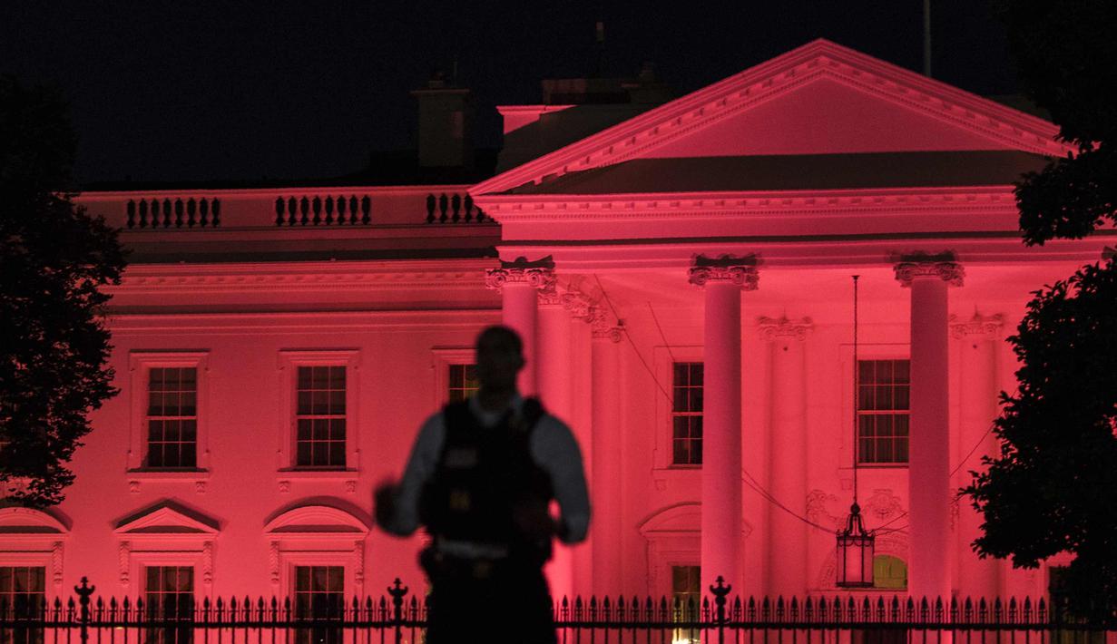 Petugas berjaga di depan Gedung Putih yang dihiasi cahaya warna pink sebagai tanda kesadaran Kanker Payudara di Washington, DC (1/10). (AFP Photo/Andrew Caballero Reynolds)
