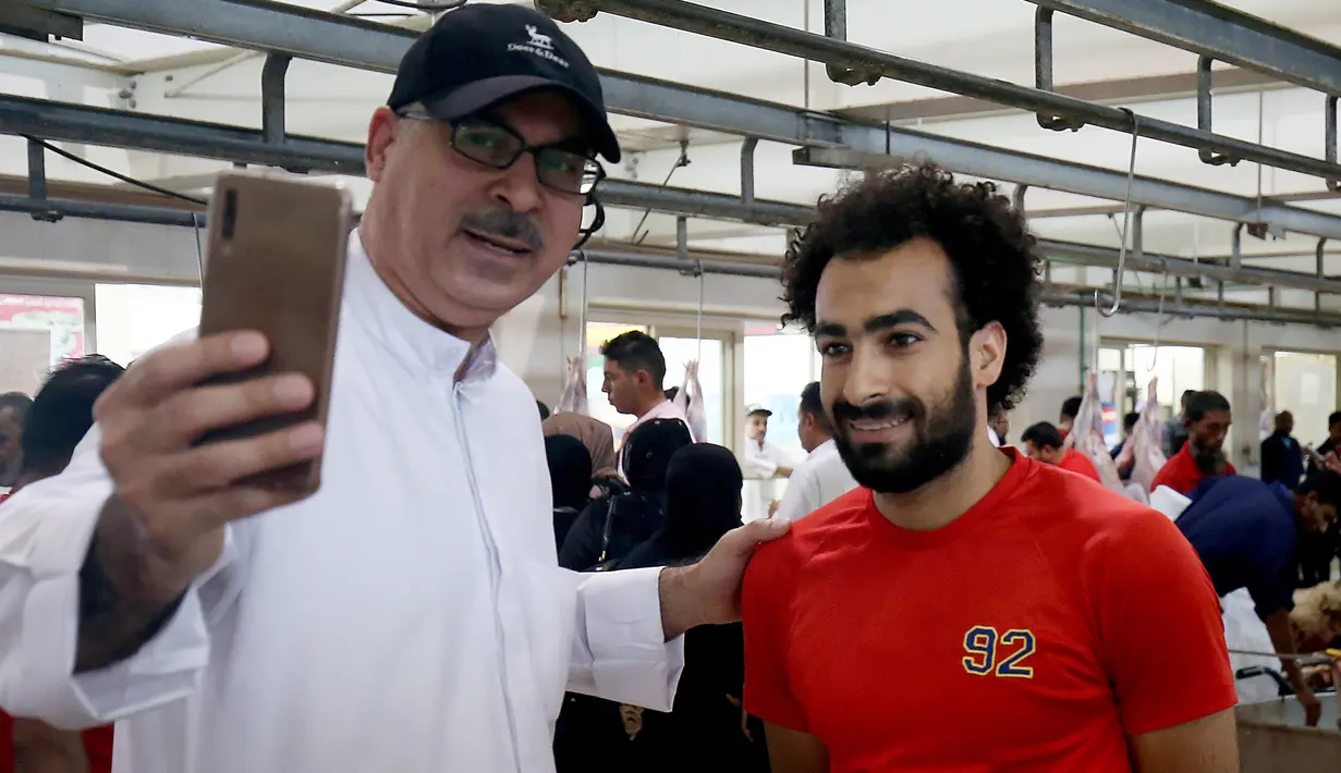 Seorang lelaki Kuwait berselfie dengan tukang daging Mesir Mohammad Ibraheem yang mirip dengan pemain Liverpool Mohamed Salah  di sebuah rumah jagal hewan di Kota Kuwait (13/8/2019). (AFP Photo/Yasser Al-Zayyat)