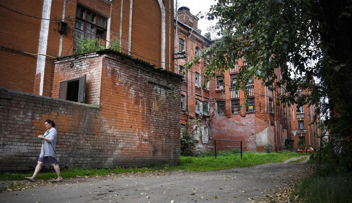 Seorang wanita berjalan melewati bangunan asrama pekerja pabrik tekstil Proletarka di Kota Tver, Rusia, 8 Agustus 2020. Zaman keemasan Proletarka diakhiri dengan pecahnya Uni Soviet dan datangnya ekonomi pasar yang membuka perbatasan bagi tekstil murah dari Tiongkok. (Alexander NEMENOV/AFP)