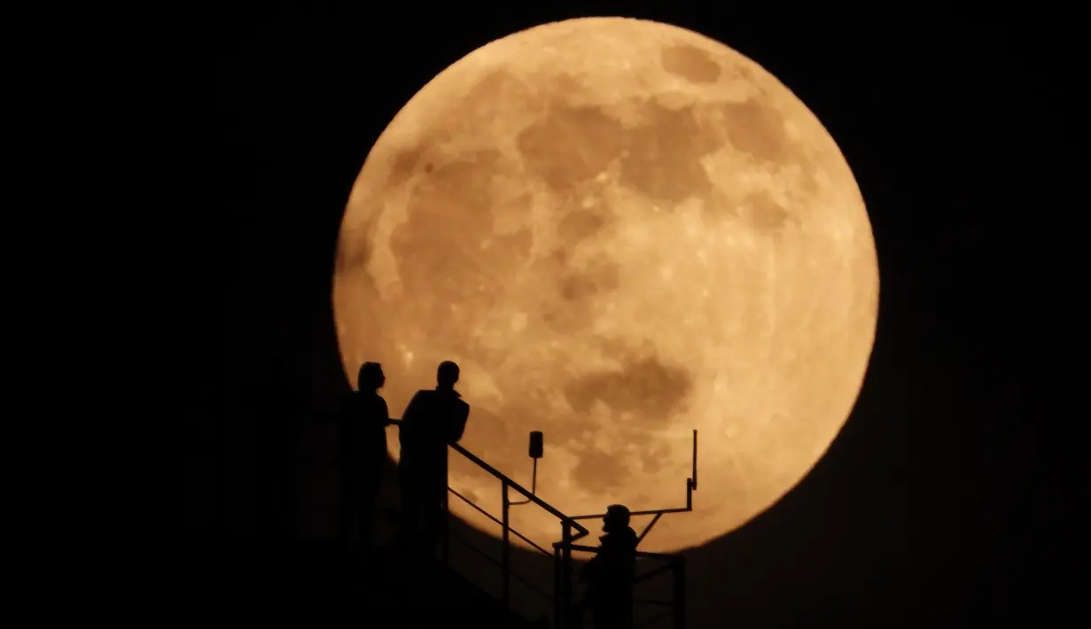 Siluet orang-orang saat bulan hampir purnama muncul di atas langit di Grozny, Rusia, Minggu (15/5/2022). (AP Photo/Musa Sadulayev)