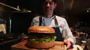Chef dari restoran The Oak Door, Patrick Shimada berpose dengan burger raksasa di hotel Grand Hyatt Tokyo, Senin (1/4). Golden Giant Burger dibuat untuk memperingati penobatan Putra Mahkota Naruhito pada 1 Mei 2019 dan menandai awal era 'Reiwa' bagi Jepang. (CHARLY TRIBALLEAU/AFP)