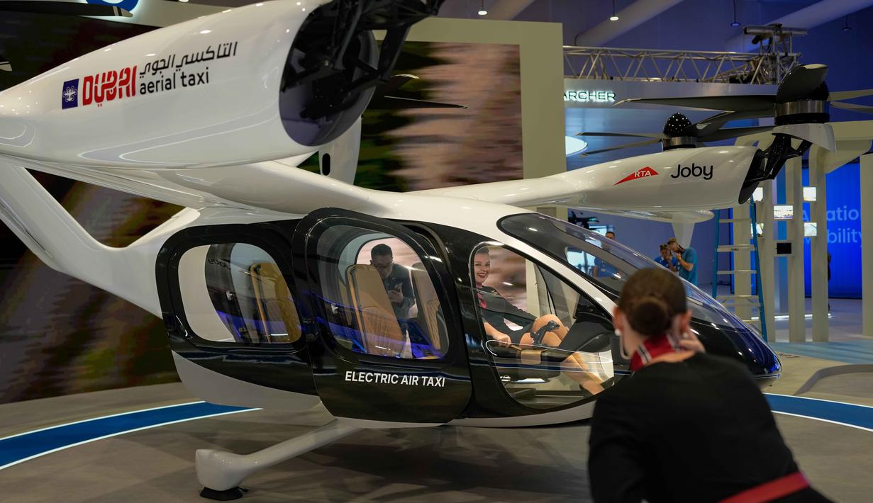 Dengan nomor registrasi N544JX, taksi udara listrik Joby melakukan penerbangan demonstrasi berawak selama Pameran Udara Dubai (Dubai Airshow) 2025. Tampak dalam foto, seorang wanita berfoto saat duduk di dalam taksi udara pada Pameran Udara Dubai, Uni Emirat Arab, Selasa 18 November 2025. (AP Photo/Altaf Qadri)