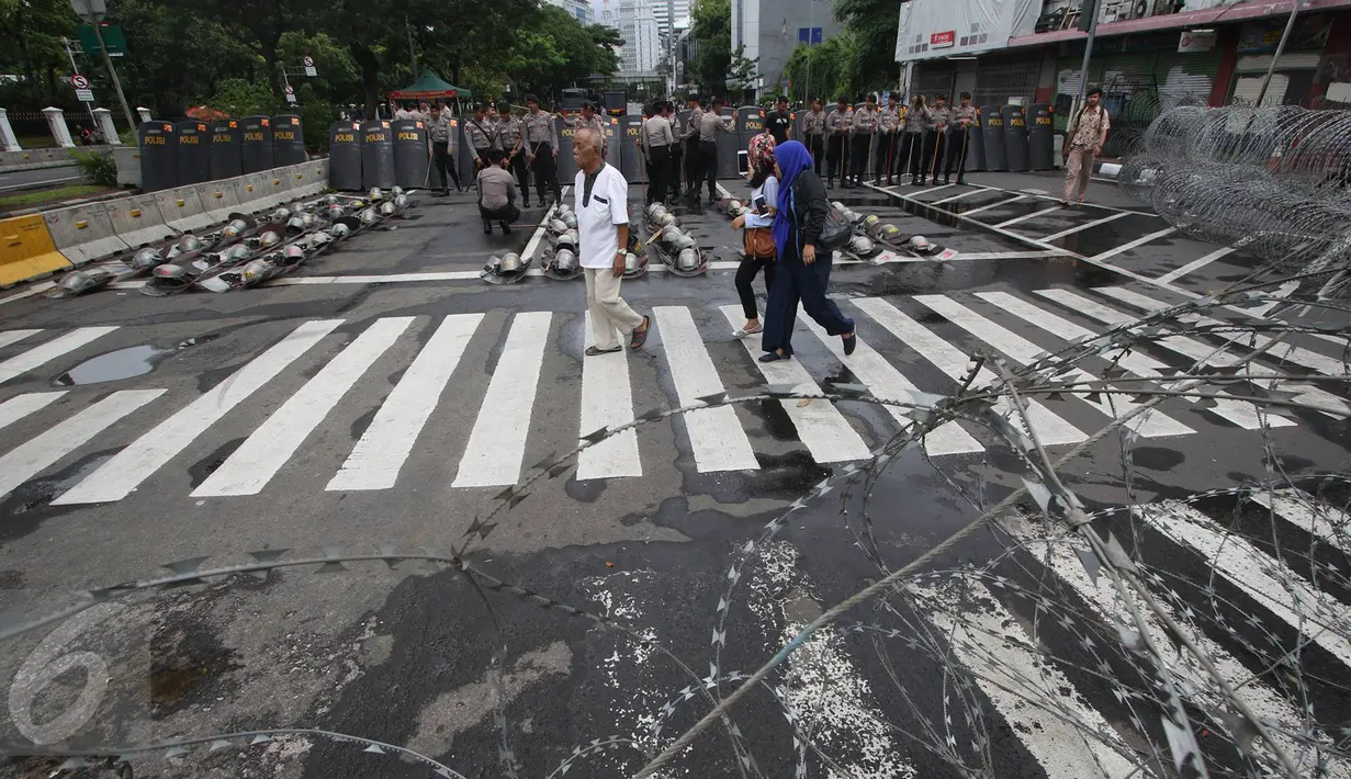 Pejalan kaki melintas dekat penjagaan ketat aparat kepolisian di sekitar Istana Negara, Jakarta, Jumat (31/3). Dalam upaya antisipasi ricuh aksi 31 Maret, polisi menutup seluruh akses jalan menuju Istana Negara. (Liputan6.com/Immanuel Antonius)