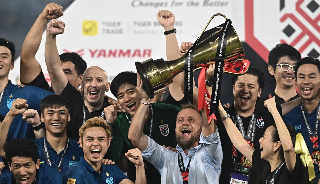 Pelatih timnas Thailand Alexandre Polking (tengah) mengangkat trofi saat para pemain merayakan gelar juara Piala AFF 2022 usai menaklukkan Vietnam dalam laga final di Stadion Thammasat, Pathum Thani, Senin (16/1/2023). Timnas Thailand keluar sebagai juara usai menang dengan skor 1-0. (Lillian SUWANRUMPHA / AFP)