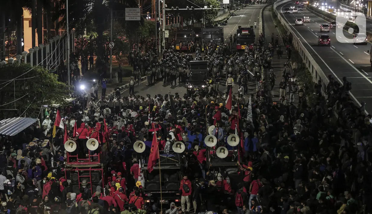 Mahasiswa dan elemen buruh bertahan hingga malam saat aksi di depan Gedung DPR/MPR/DPD, Jakarta, Kamis (16/7/2020). Dalam aksinya, mereka menolak pengesahan RUU Cipta Kerja atau Omnibus Law yang saat ini sedang dibahas DPR bersama pemerintah. (Liputan6.com/Johan Tallo)