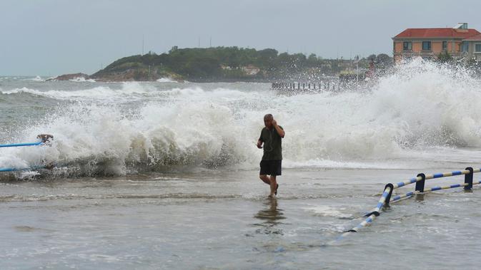 Seorang pria berjalan saat ombak besar yang disebabkan Topan Yagi di sepanjang pantai laut di Qingdao di provinsi Shandong timur China (13/8). Menurut Kantor Berita Xinhua, Topan Yagi memiliki kecepatan hingga 102 kilometer per jam. (AFP Photo)