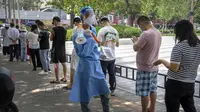 Seorang pekerja yang mengenakan pakaian pelindung dan membawa megafon memegang selembar dengan kode QR untuk orang-orang yang mengantre untuk tes virus corona COVID-19 di tempat pengujian pada hari ketiga pengujian massal untuk jutaan penduduk di Distrik Chaoyang, Beijing, China, 15 Juni 2022. (AP Photo/Mark Schiefelbein)