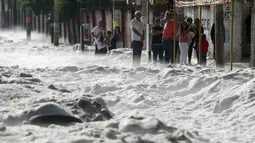 Sejumlah warga berdiri di trotoar melihat salju tebal yang menutupi jalan di wilayah timur Guadalajara, Jalisco, Meksiko (30/6/2019). Pemerintah daerah setempat mengatakan sebanyak 200 rumah rusak dan puluhan kendaraan tersapu di dalam kota dan beberapa distrik di sekitarnya. (AFP Photo/Ulises Ruiz)