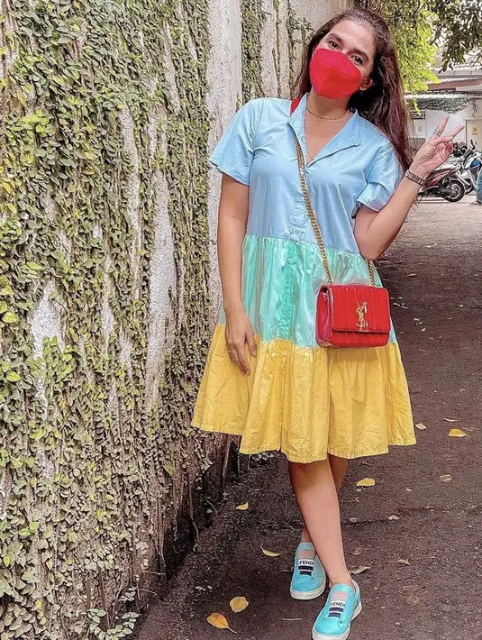 Dress selutut masih menjadi fashion andalan Ussy. Kali ini ia memilih dress ruflle colorful. Serasi dengan warna sepatunya. Sling bag merah dari brand YSL melengkapi penampilannya. (Dok. Instagram @ussypratama)