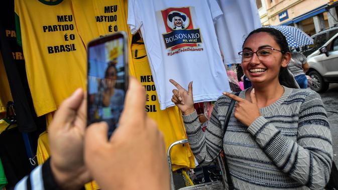 Seorang wanita berfoto dengan kaus bergambar Capres Brasil, Jair Bolsonaro dari sayap kanan di sebuah toko pinggir jalan yang populer di Sao Paulo, 8 Oktober 2018. Bolsonaro unggul dalam penghitungan suara pemilu putaran pertama. (AFP/NELSON ALMEIDA)