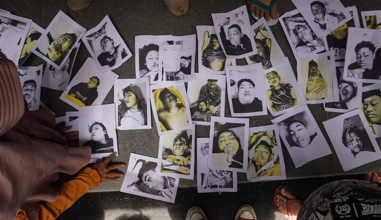 Orang-orang yang mencari anggota keluarganya memeriksa foto-foto korban kerusuhan Stadion Kanjuruhan yang disediakan oleh relawan untuk membantu mereka mengidentifikasi kerabat mereka di Malang, Jawa Timur, Minggu (2/10/2022).  Warga yang kehilangan anggota keluarganya dalam tragedi kerusuhan tersebut diminta untuk melapor ke posko yang ada. (AP Photo/Dicky Bisinglasi)