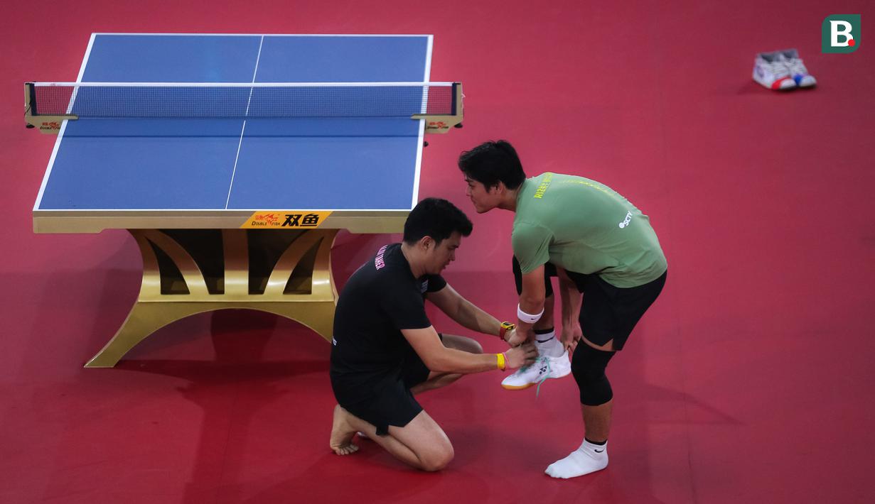 Selebritas Aldi Taher memakaikan sepatu ke Rizky Billar saat laga tenis meja Turnamen Olahraga Selebriti Indonesia (TOSI) di GOR UNJ, Jakarta, Minggu (16/07/2023). Aldi Taher kalah tiga set langsung dari Rizky Billar dengan skor 12-21, 15-21, 11-21. (Bola.com/Bagaskara Lazuardi)