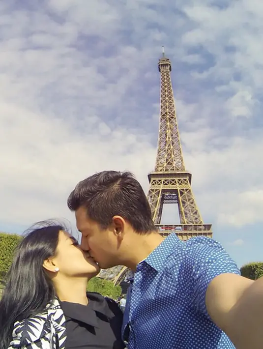 Pasangan suami istri Christian Sugiono dan Titi Kamal berciuman mesra di depan menara Eiffel, Paris. "Obligatory selfie kiss in front of Eiffel Tower" tulis Christian dalam akun instagramnya @csugiono. (Photo : Instagram)