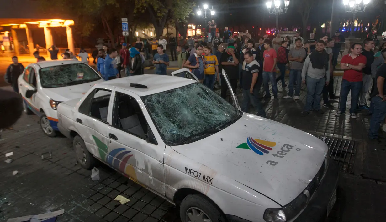 Massa melihat dua mobil milik sebuah stasiun TV yang rusak dalam unjuk rasa kenaikan harga BBM di Monterrey, Meksiko, Kamis (5/1). Unjuk rasa tersebut merupakan protes atas kenaikan harga BBM hingga 20% yang dilakukan pemerintah. (Julio Cesar Aguilar/AFP)