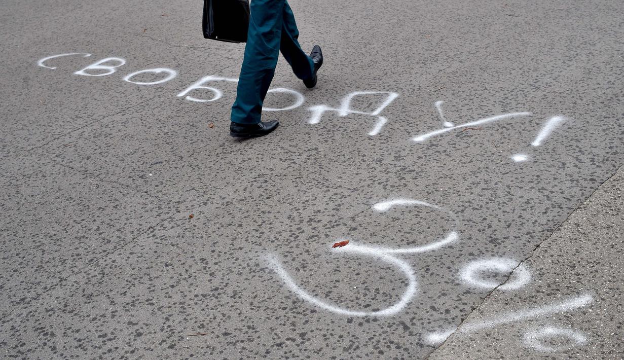 Seorang pria berjalan di halaman aspal yang dilukis dengan tulisan "Kebebasan! 3%", mengacu pada Alexander Lukashenko, yang dijuluki "Sasha 3 persen" dalam ejekan pada peringkat populernya yang seharusnya rendah, di Minsk (25/8/2020). (AFP/Sergei Gapon)