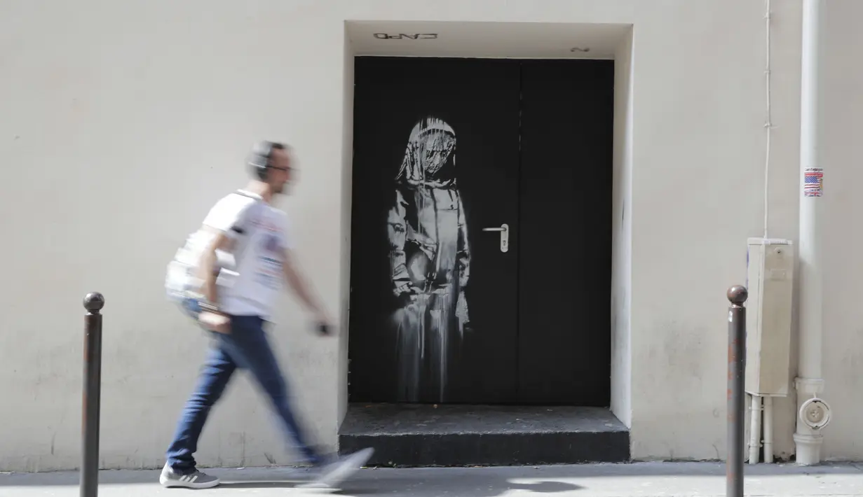 Seorang pria berjalan melewati mural yang diduga karya seniman sekaligus aktivis Banksy di Paris, Prancis, Minggu (24/6). Seniman jalanan misterius asal Inggris itu membuat mural bertema migrasi. (THOMAS SAMSON/AFP)