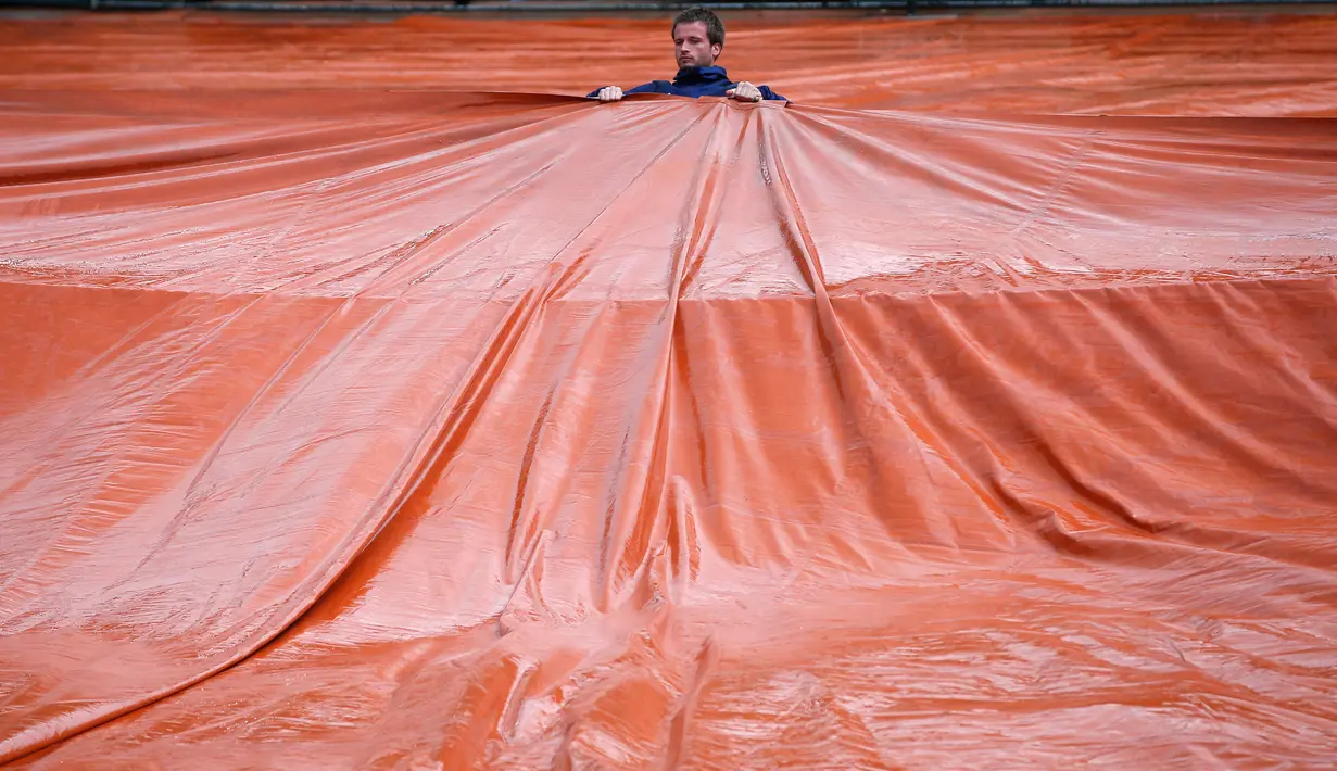 Seorang pekerja stadion menarik penutup lapangan usai pertandingan perempat final Perancis Terbuka ditunda karena hujan di stadion Roland Garros, Paris (6/6). (AP/Thibault Camus)