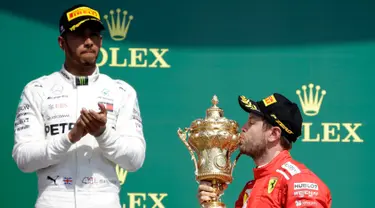 Pembalap Ferrari, Sebastian Vettel (benar) mencium piala di depan pembalap Mercedes, Lewis Hamilton (kiri) saat menjuarai F1 GP di Sirkuit Silverstone, Inggris, Minggu (8/7). Vettel mengungguli Lewis Hamilton dan Kimi Raikkonen. (AP Foto/Luca Bruno)