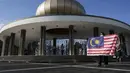 Seorang pengunjung berpose dengan bendera nasional Malaysia di depan Monumen Nasional saat perayaan Hari Nasional ke-64 untuk memperingati kemerdekaan Malaysia dari penjajahan Inggris di Kuala Lumpur, Malaysia, Selasa (31/8/2021). (AP Photo/Vincent Thian)