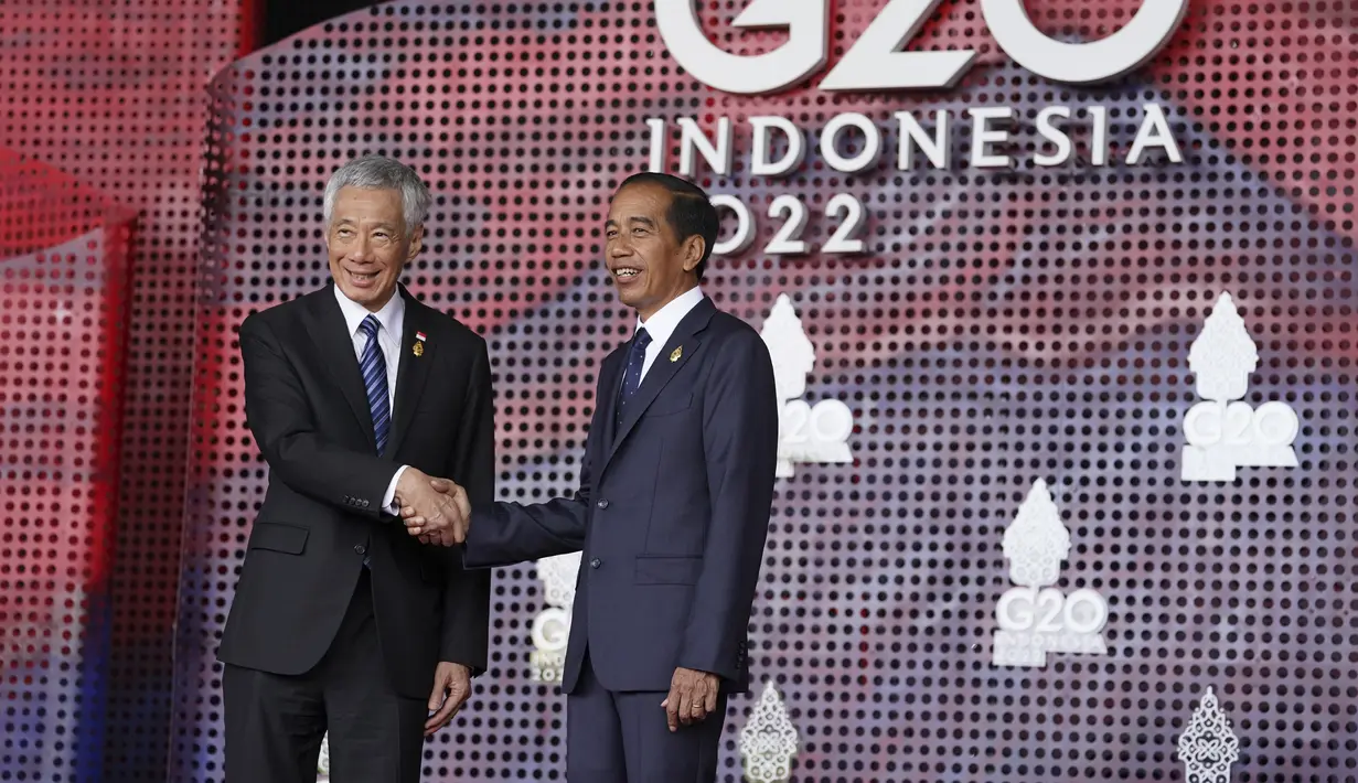 Perdana Menteri Singapura Lee Hsien Loong menyapa Presiden Indonesia Joko Widodo atau Jokowi yang menyambutnya pada hari pertama Konferensi Tingkat Tinggi (KTT) G20 di Nusa Dua, Bali, Selasa (15/11/2022) pagi. Setidaknya total 17 kepala negara G20 akan menghadiri KTT dua hari ini. (Kevin Lamarque/Pool via AP)
