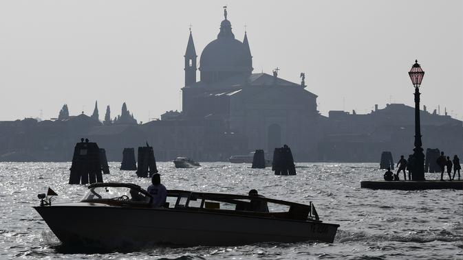 Gereja Santa Croce terlihat di pulau Giudecca dan orang-orang berdiri di Punta della di Venesia (4/11/2019). Punta della Dogana adalah sebuah museum seni di salah satu bangunan pabean lama Venesia, Dogana da Mar. (AFP Photo/Miguel Medina)
