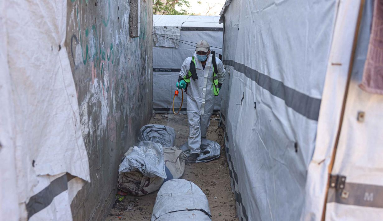 Angka tersebut mencakup sekitar 90% dari total populasi Gaza, di mana banyak yang telah berpindah tempat tinggal beberapa kali akibat konflik yang berlangsung. Tampak dalam foto, seorang pengungsi Palestina menyemprotkan cairan disinfektan pada jalan setapak dan tenda-tenda untuk membasmi serangga dan hewan pengerat di kamp pengungsian Khan Yunis, Jalur Gaza Selatan pada Rabu 22 April 2026. (Bashar Taleb/AFP)