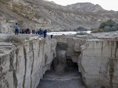Warga Israel menyaksikan banjir bandang terjadi menyusul hujan lebat di gurun Negev di sebelah timur kota Dimona Israel pada 26 Desember 2022. Hujan lebat mengguyur Israel pada hari Senin (26/12) membanjiri jalan-jalan kota, memicu banjir bandang di dasar sungai gurun yang kering dan membasahi daerah pedesaan karena suhu turun ke level terendah musim ini. (AFP/Menahem Kahana)