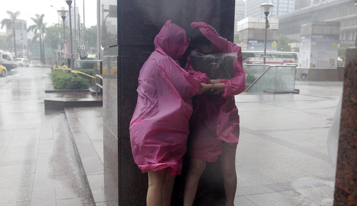 Dua wanita berlindung di dinding untuk menghindari angin kencang yang disebabkan topan Dujuan di Taipei, Taiwan, Senin (28/9). Ribuan orang diungsikan untuk menghadapi topan raksasa Dujuan yang diprediksikan akan menyerang Taiwan.(REUTERS/Pichi Chuang)