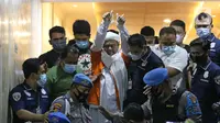 M Rizieq Shihab (tengah) digiring petugas saat meninggalkan gedung Ditreskrimum Polda Metro Jaya, Jakarta, Minggu dini hari (13/12/2020). Rizieq Shihab ditahan setelah menjalani pemeriksaan sebagai tersangka penghasutan dan kerumunan di tengah pandemi COVID-19. (Liputan6.com/Helmi Fithriansyah)
