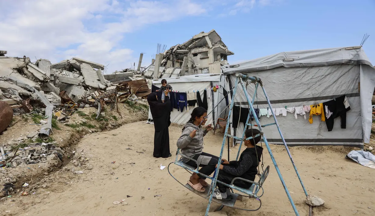 Pembentukan dua badan tersebut dinyatakan dalam sebuah pernyataan pada Jumat (16/1/2026). Tampak dalam foto, para pengungsi Palestina yang tinggal di antara reruntuhan rumah dan bangunan yang hancur akibat serangan militer Israel selama lebih dari dua tahun di wilayah Gaza, bermain ayunan di luar tenda mereka, di kamp pengungsi Jabalia, di bagian utara Jalur Gaza pada Sabtu 17 Januari 2026. (Omar AL-QATTAA/AFP)