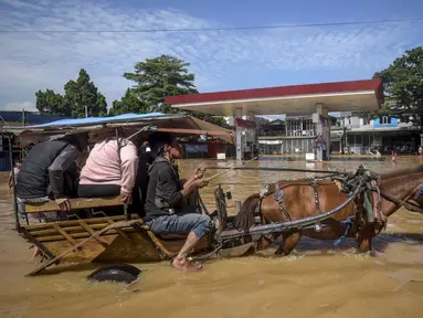 Sebuah kereta kuda mengangkut penumpang melewati jalan yang tergenang banjir melewati sebuah Stasiun Pengisian Bahan Bakar Umum (SPBU) di Bandung, Jawa Barat pada Jumat 5 Desember 2025. Banjir melanda berbagai wilayah di Kabupaten Bandung. Curah hujan tinggi pada Kamis (4/12/2025) sore hari, mengakibatkan aliran sungai Citarum meluap dan merendam sejumlah pemukiman hingga hari ini. (TIMUR MATAHARI/AFP)