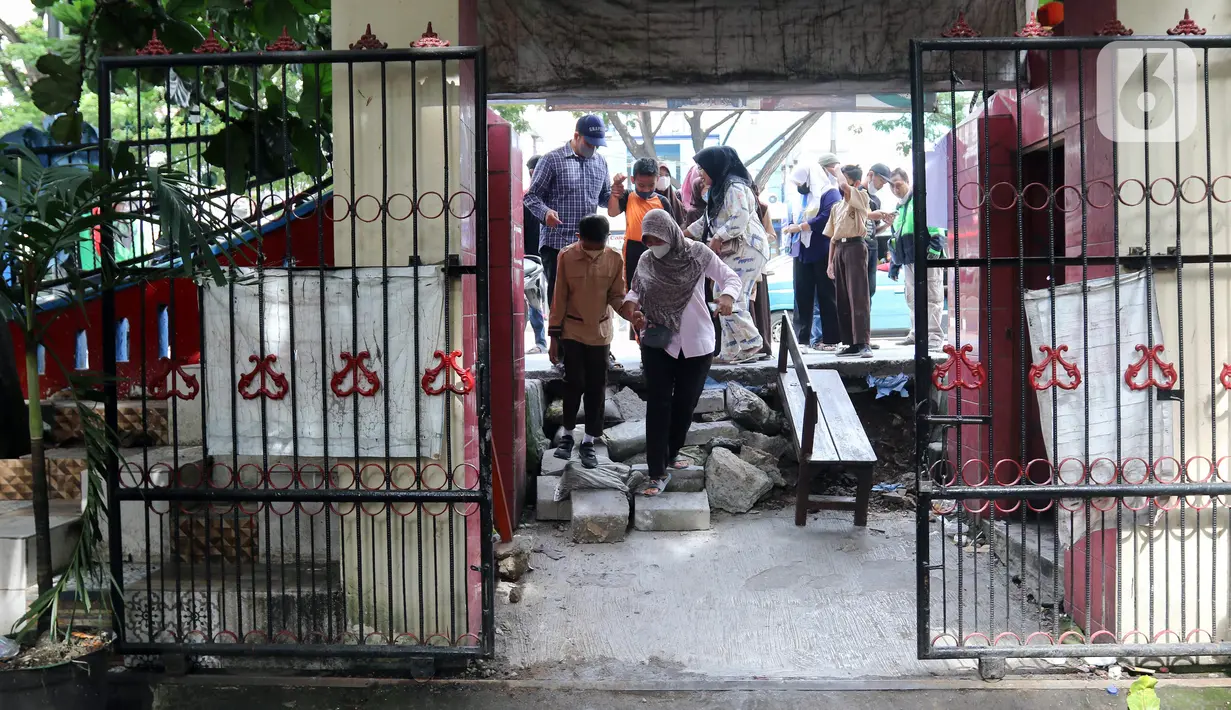 Sejumlah siswa berjalan masuk melintasi jalan darurat yang dibuat pihak sekolah di SDN Pondok Cina 1, Depok, Jawa Barat, Rabu (9/11/2022). Pembangunan trotoar Jalan Margonda Raya yang tidak membuat jalan darurat untuk siswa tersebut menghalangi pintu masuk SDN Pondok Cina 1 serta membahayakan siswa. (Liputan6.com/Herman Zakharia)