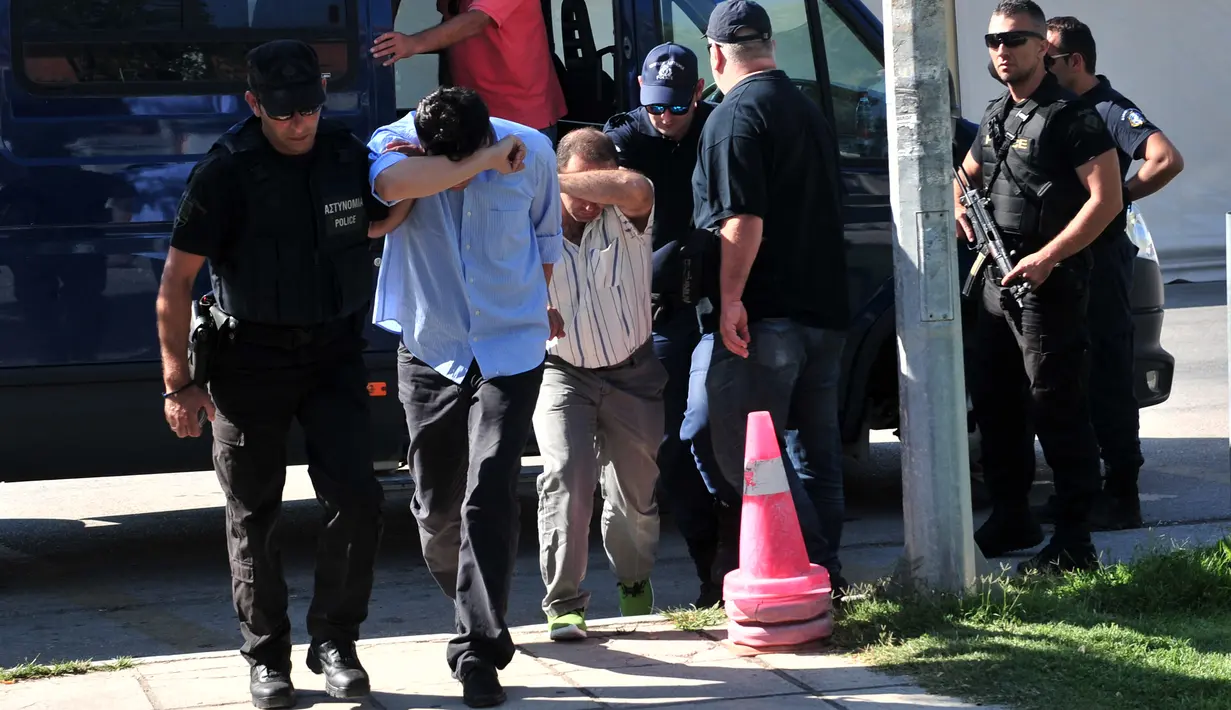 Dua dari 8 perwira militer pendukung kudeta Turki menutupi wajahnya, di Alexandroupoli, utara Yunani, Minggu (17/7). 8 pria yang terbang dengan helikopter militer Turki itu ditahan petugas keamanan Yunani karena masuk secara ilegal. (Sakis MITROLIDIS/AFP)